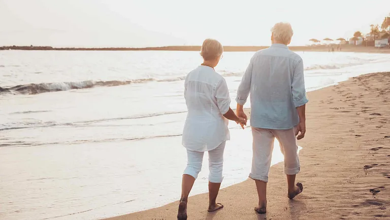 Old couple walking hand in hand on the beech